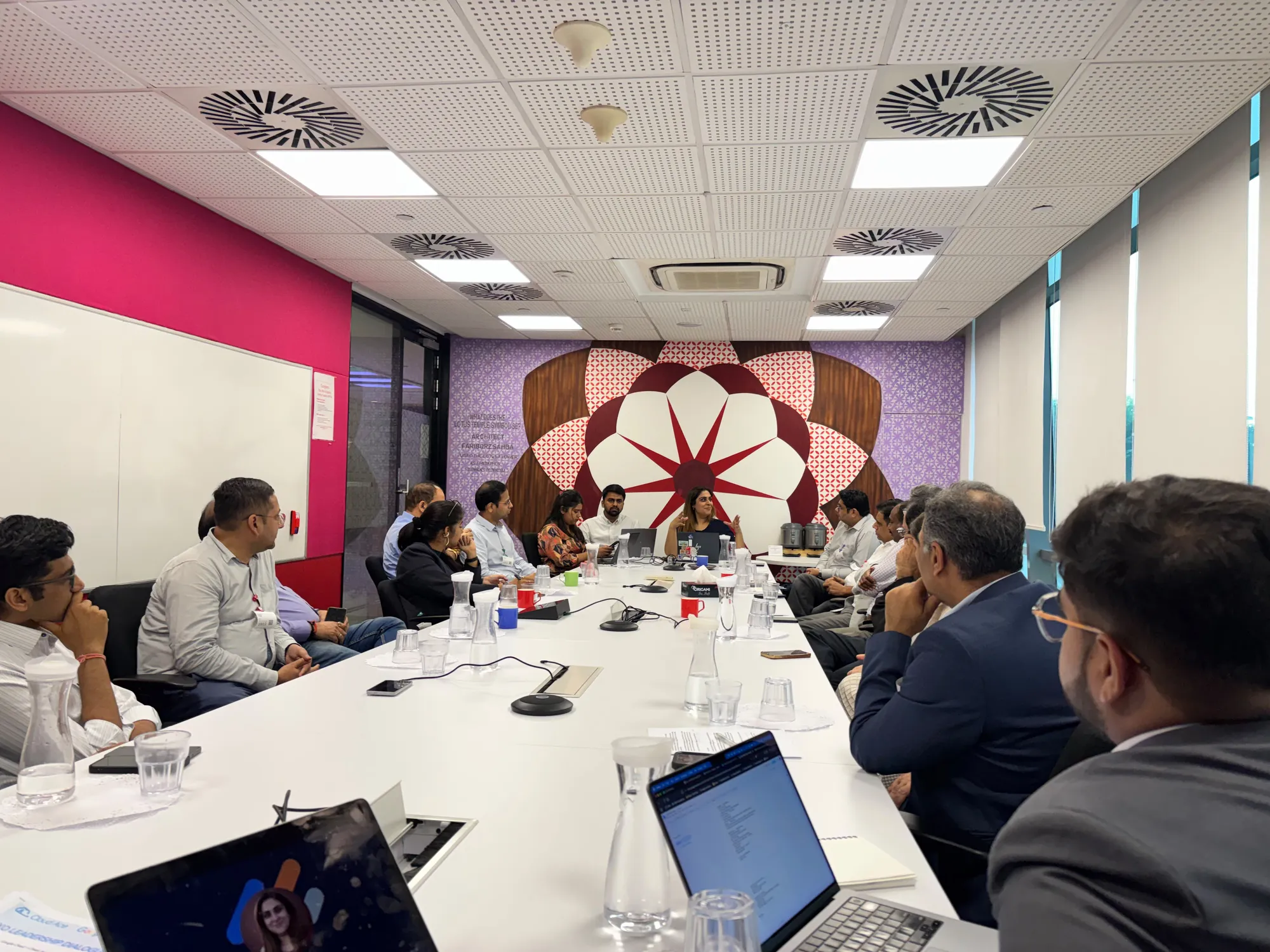 Participants around the boardroom table during the discussion, with laptops open and a colourful mural on the back wall