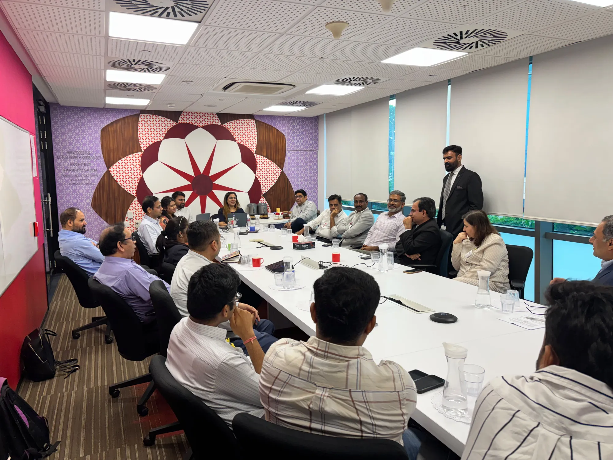 Participants listening and discussing around the boardroom table, with a host standing at the far end