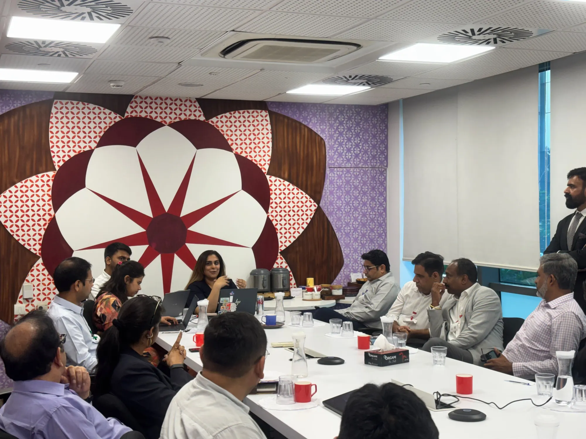 Leaders in conversation around the boardroom table, with flasks and cups on the table and a large floral mural behind